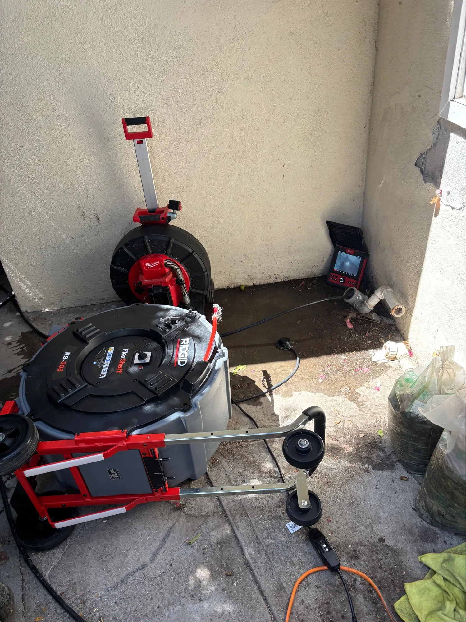 Sewer camera reel and monitor at a cleanout, the cable run into the pipe, with a drain cleaning machine in front