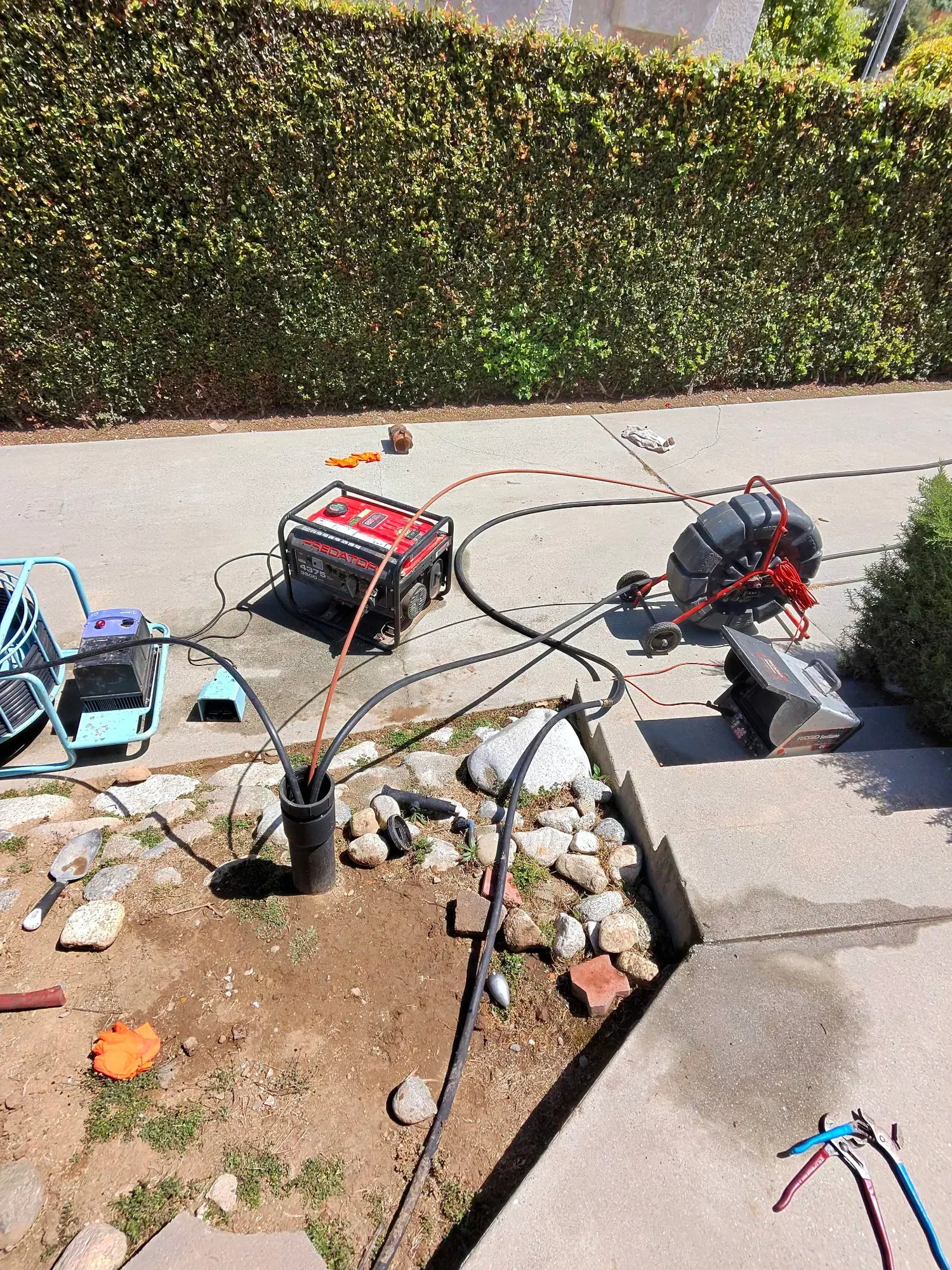 Sewer camera reel and monitor set up at an outdoor cleanout, cables run into the pipe beside a generator