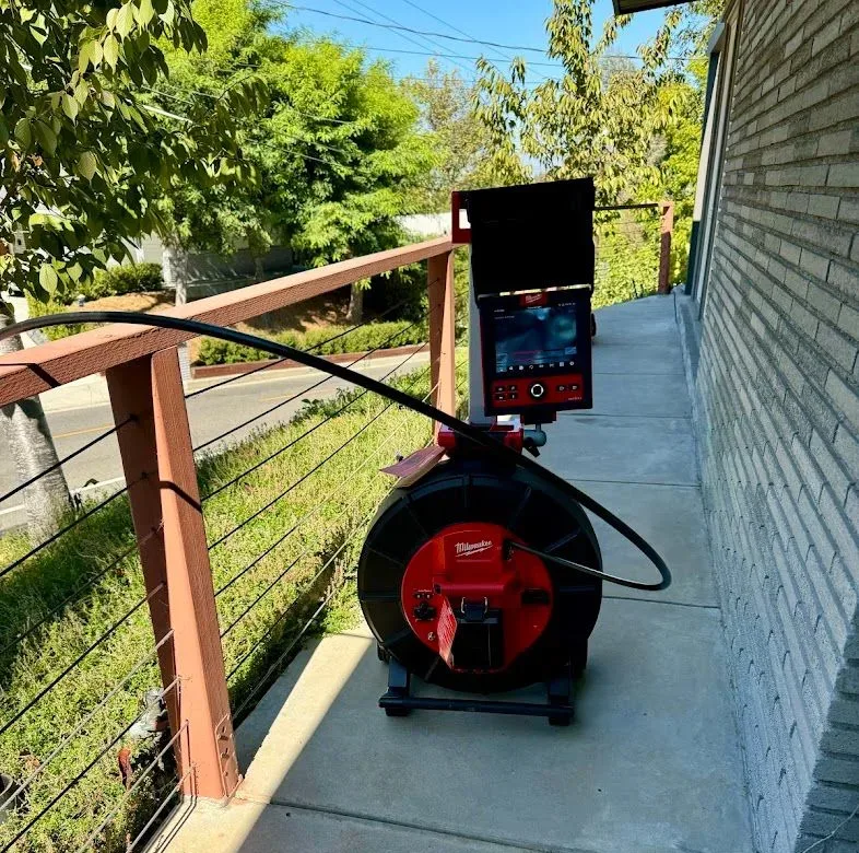 Sewer camera reel with its monitor raised, set up on a concrete walkway beside a brick wall