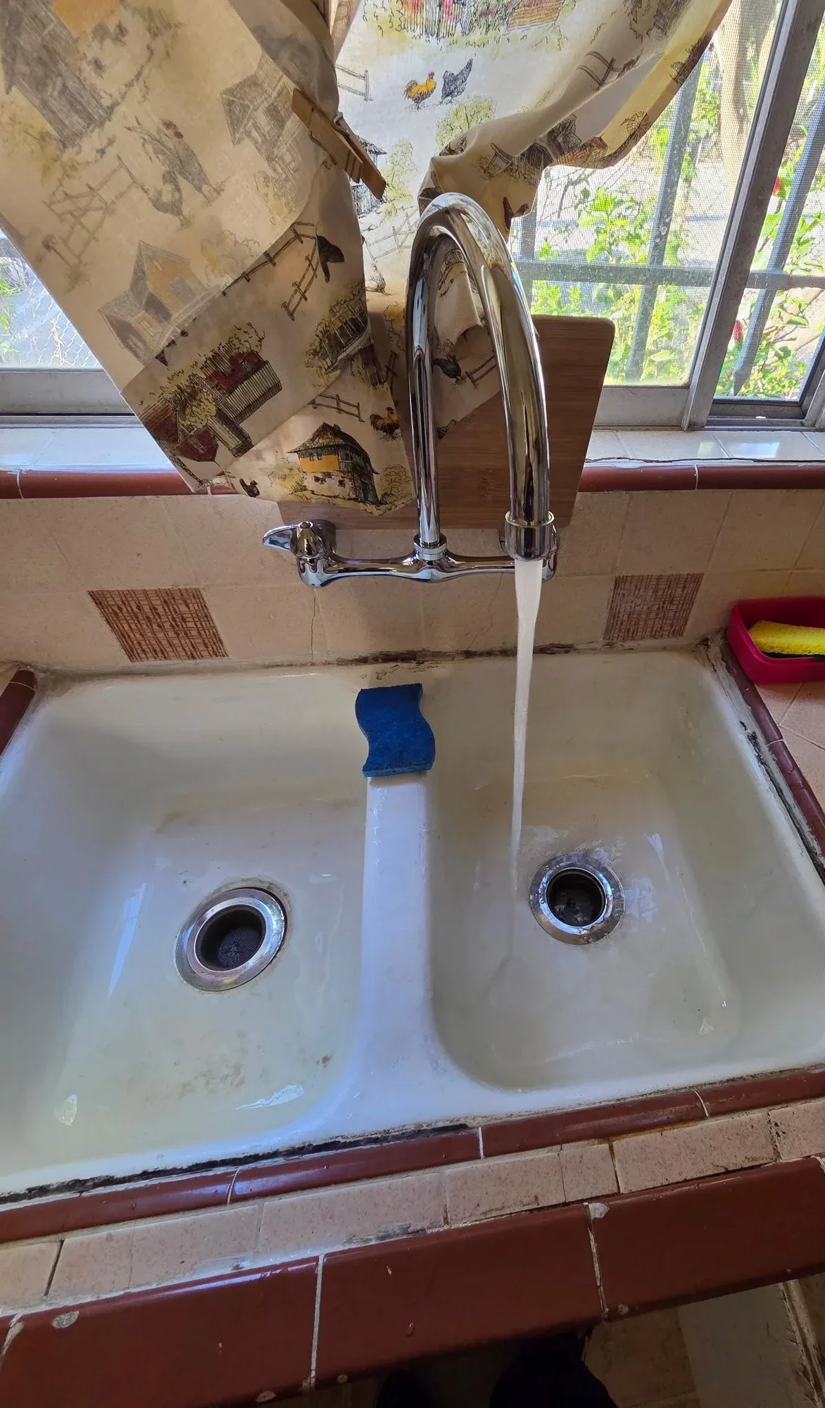 Chrome wall mounted faucet running into an older double basin kitchen sink set in tile