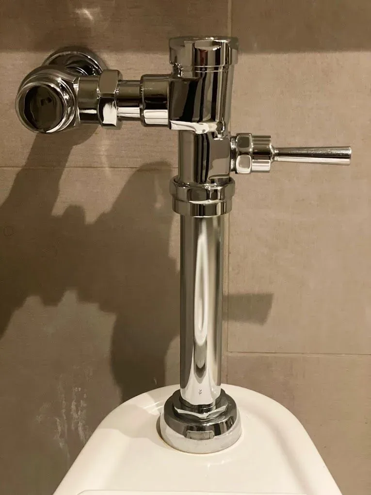 Chrome manual flush valve with a side handle against a tiled wall