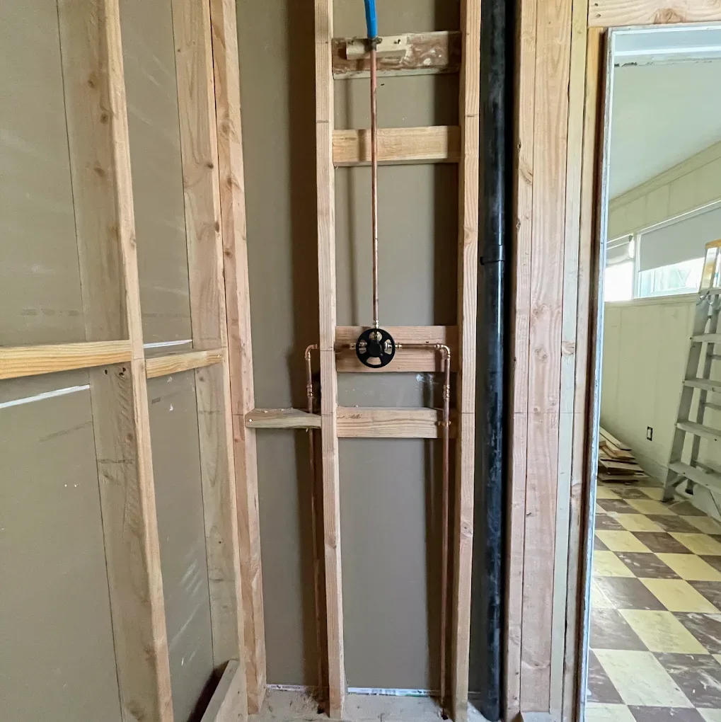 Valve and new copper water lines set between open wall studs beside a black drain pipe