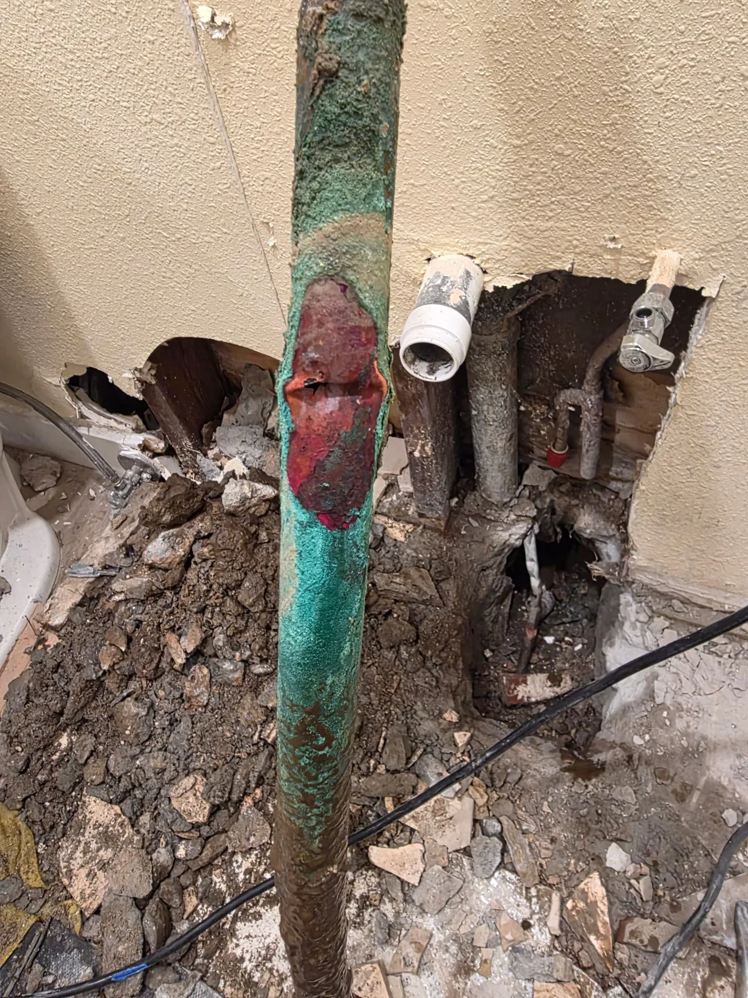 Removed copper water line, corroded green with a damaged section, in front of an opened bathroom wall