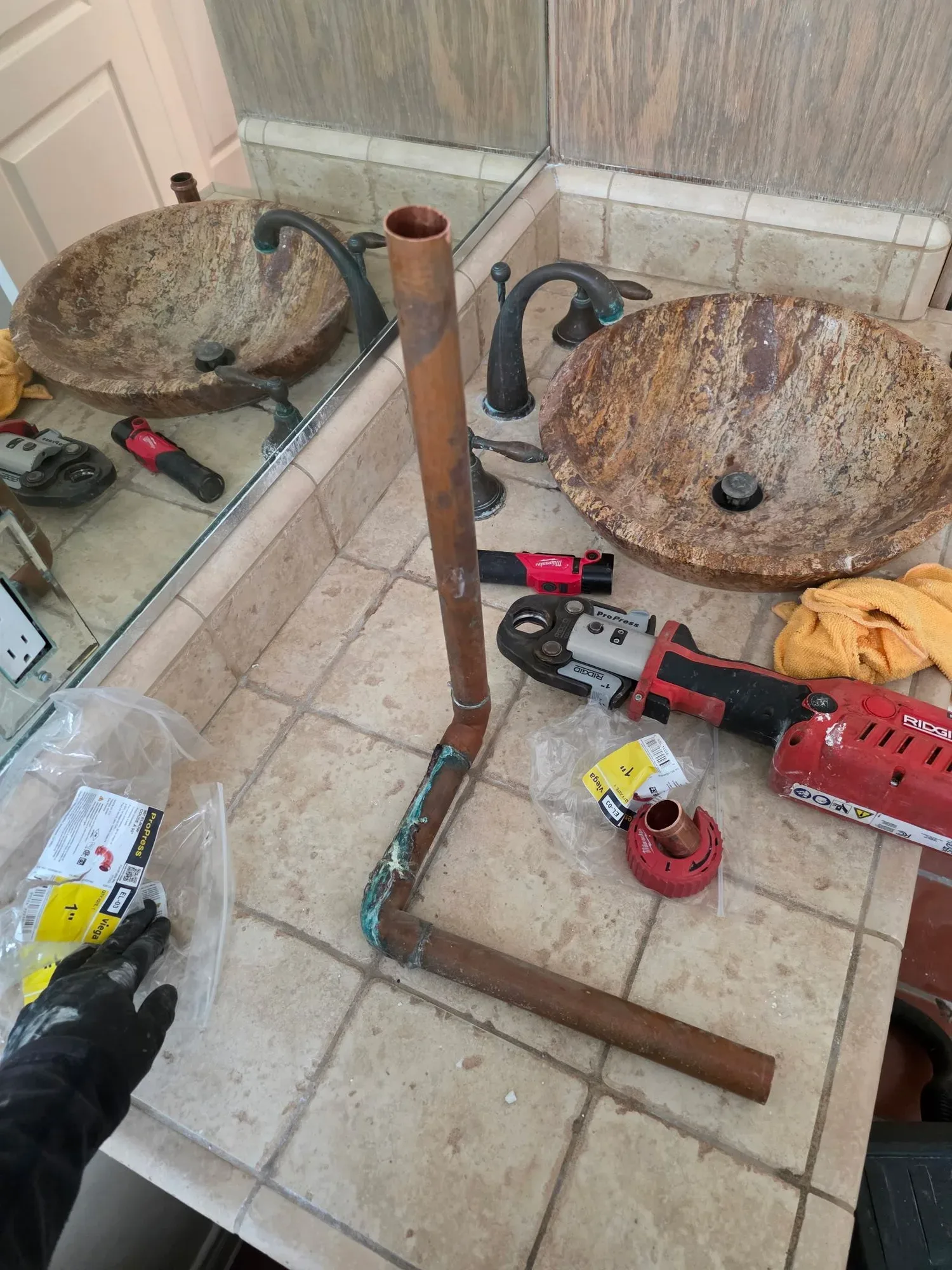 Removed copper pipe with green corrosion at the elbow on a tiled vanity, beside a press tool and fittings
