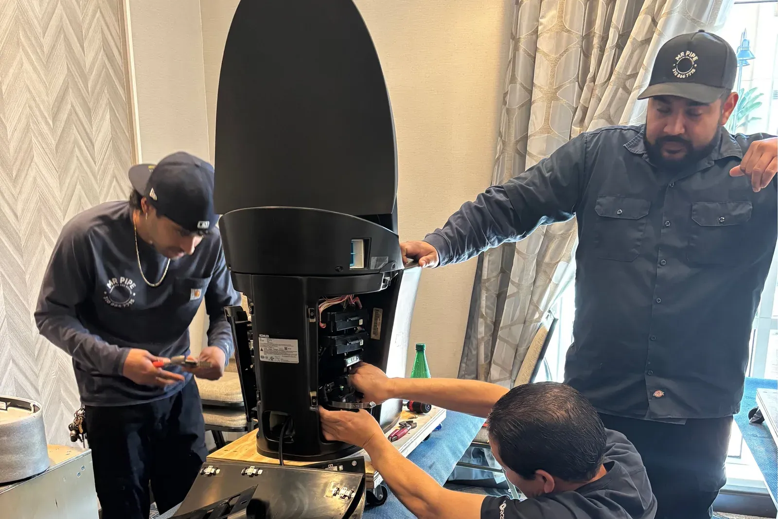 Three Mr. Pipe technicians servicing a Kohler intelligent toilet on a job