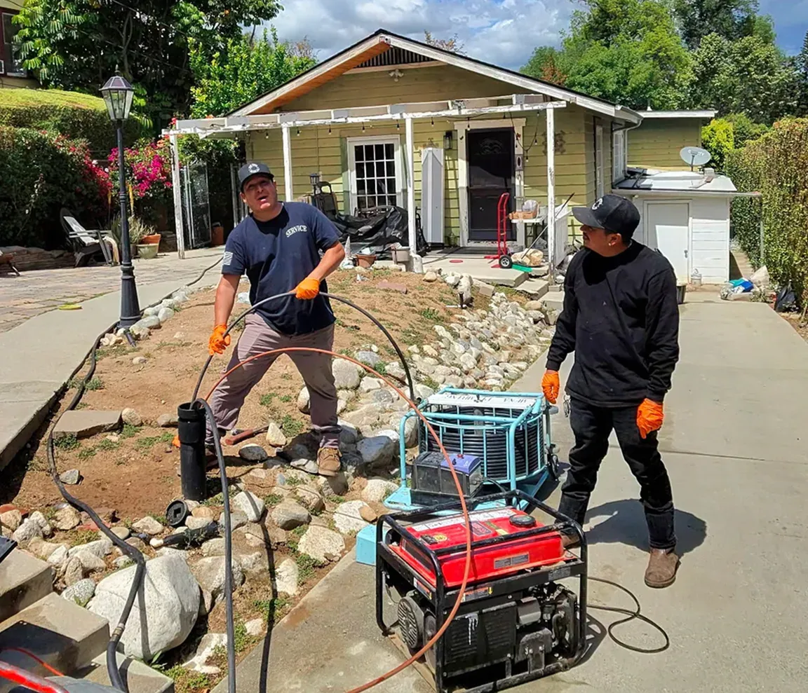 Two Mr. Pipe technicians running a cable from a front-yard drain cleanout