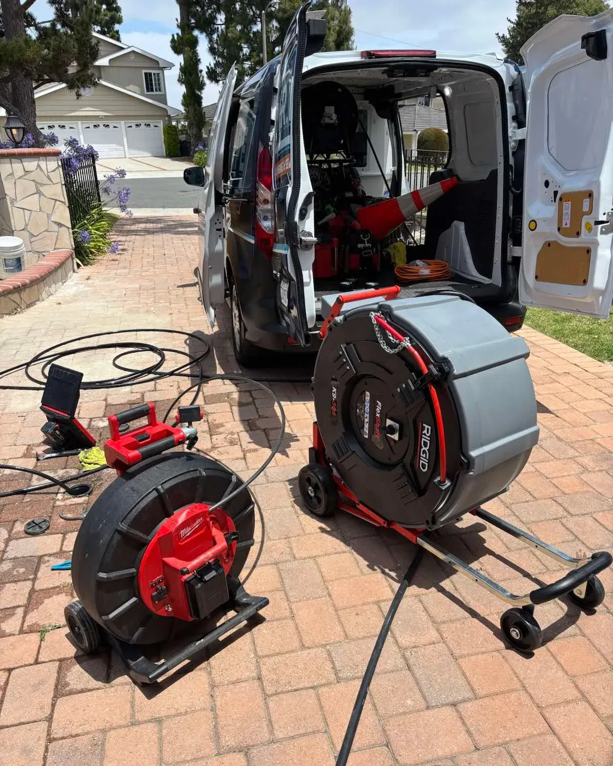 A Mr. Pipe van with its rear doors open on a driveway, a drain machine and a camera reel run out onto the pavers beside it