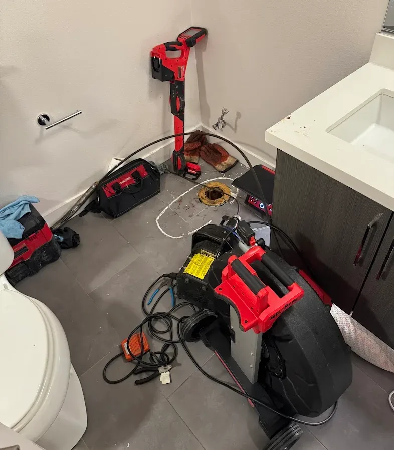 Drain-cleaning machine with its cable fed into an open toilet drain on a bathroom floor