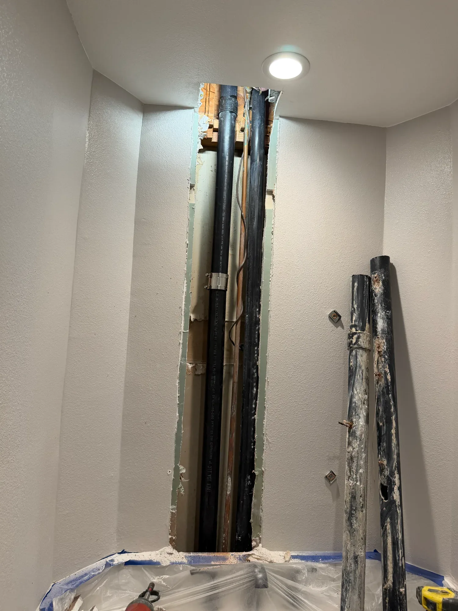 Black drain stack inside a tall opening in a bathroom wall, with old pipe sections set aside