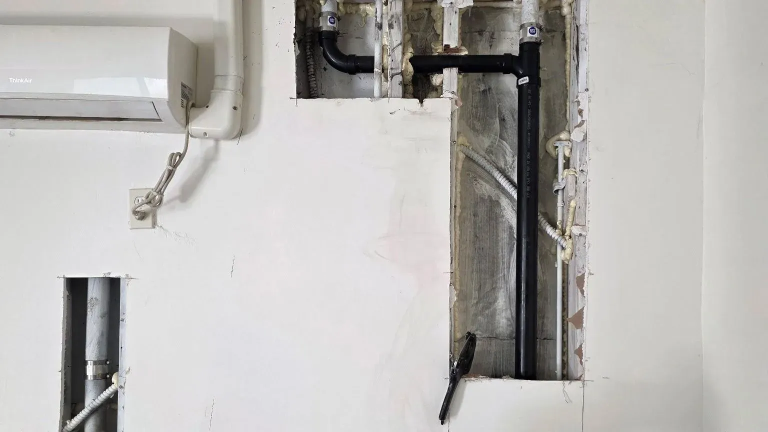 Opened drywall sections exposing drain piping inside the wall cavities during a repair