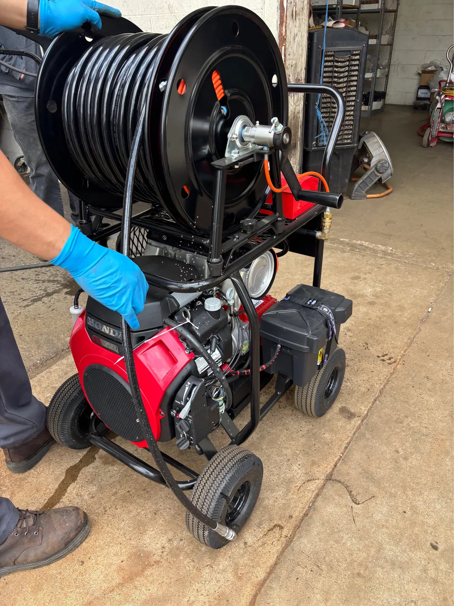 Hydro jetter with a loaded hose reel, steadied by a technician wearing blue gloves