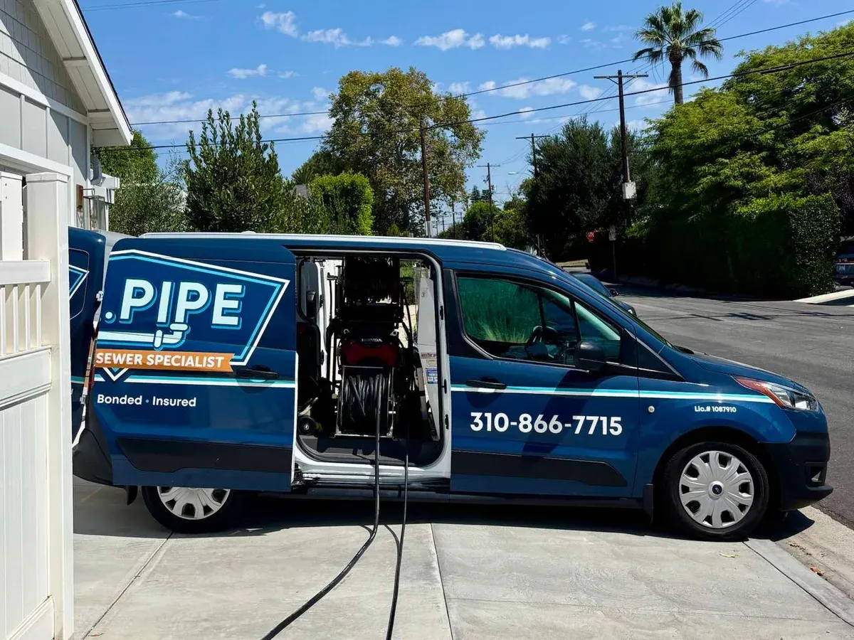 A Mr. Pipe van parked on a driveway with its side door open, the gas-powered hydro jetter and hose reel loaded inside and the jetting hose run out across the concrete