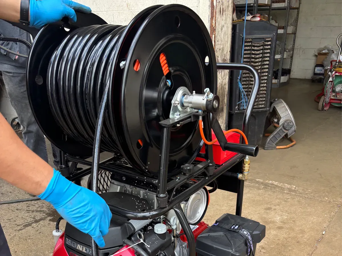 A technician in work gloves guiding the hose reel of a gas-powered hydro-jetting machine
