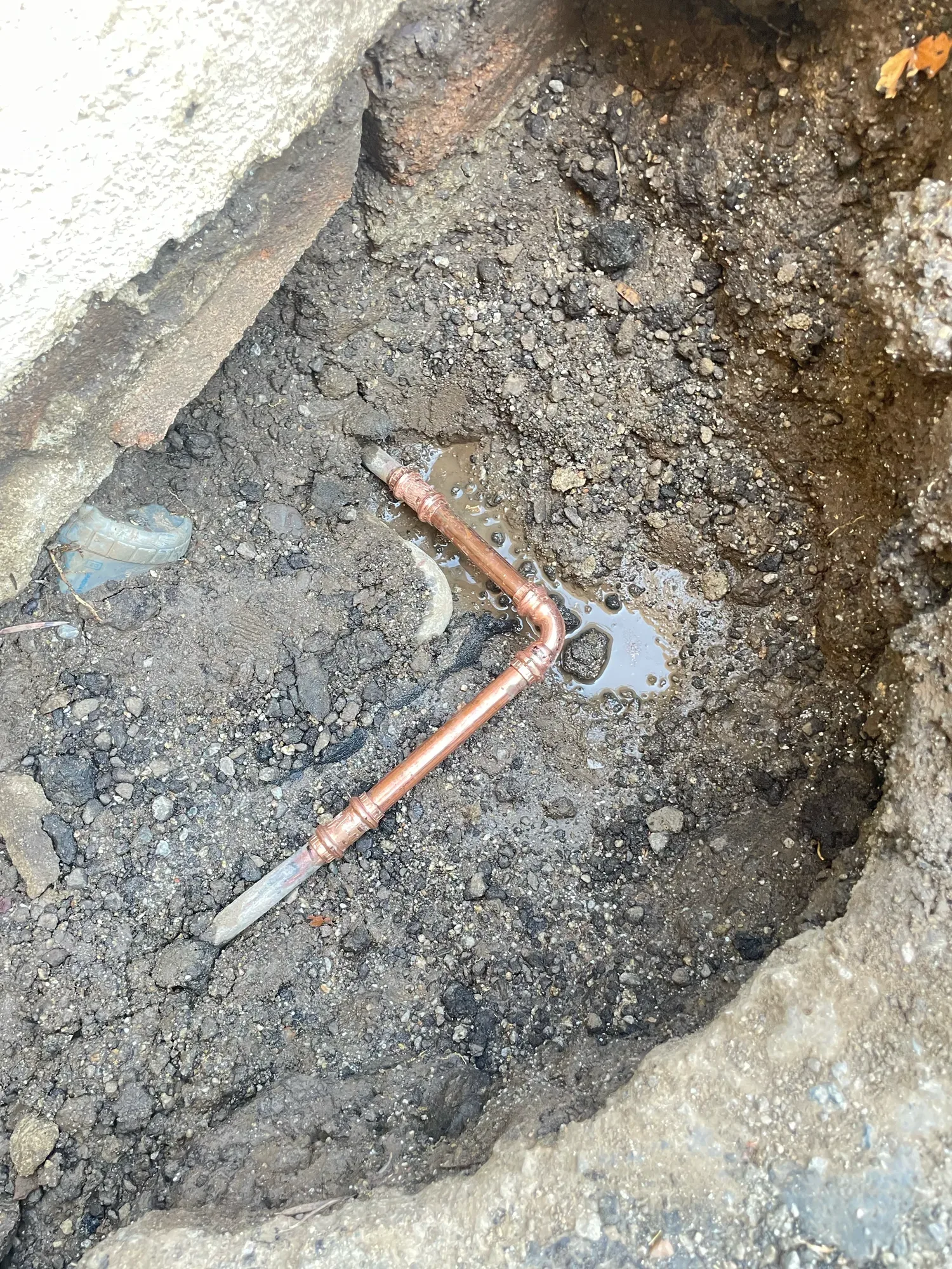 New copper elbow with pressed fittings laid in a shallow dirt excavation, with water pooled around the joint