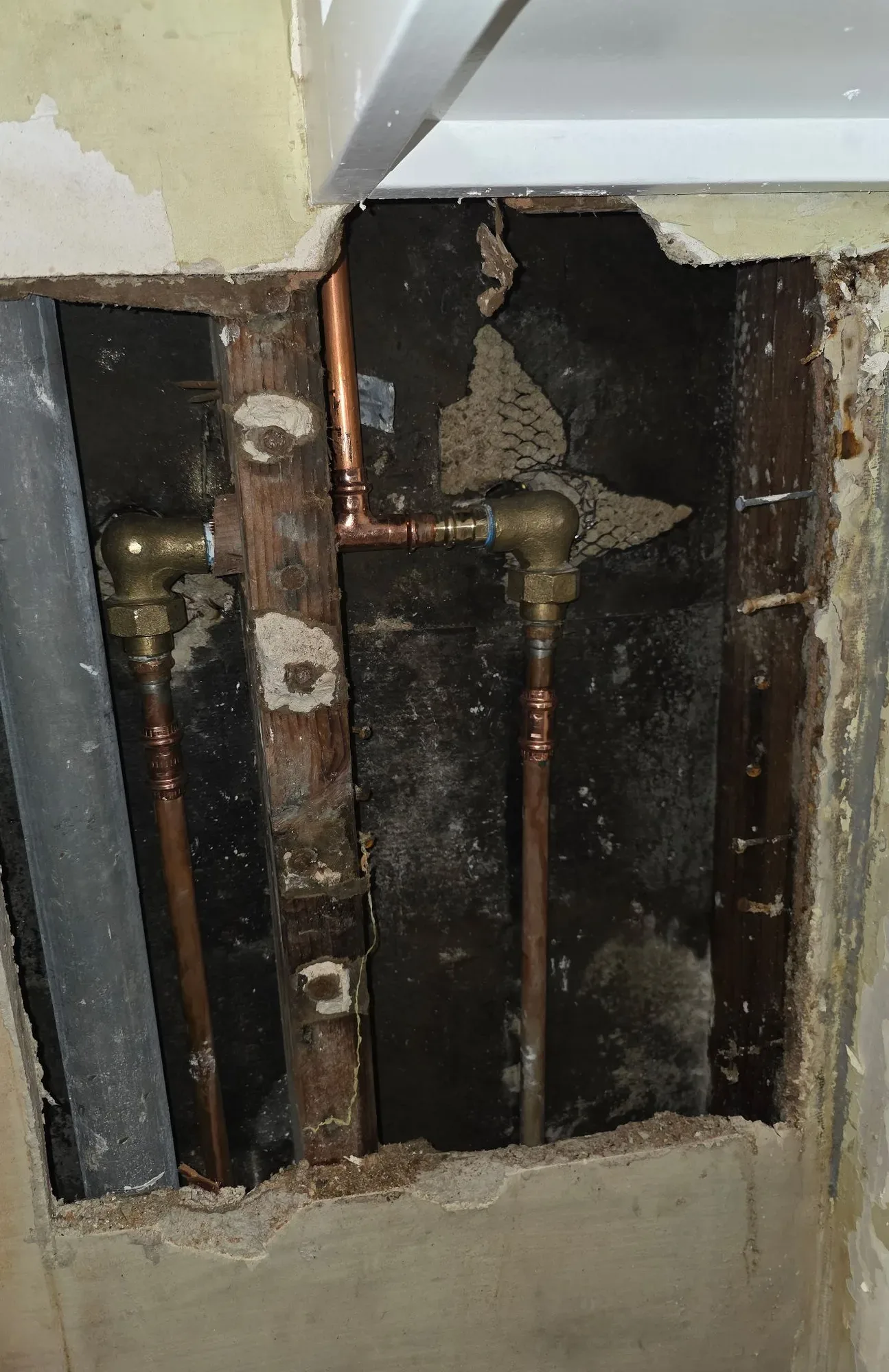 New copper water lines and brass elbows inside an opened wall cavity with dark staining on the back panel