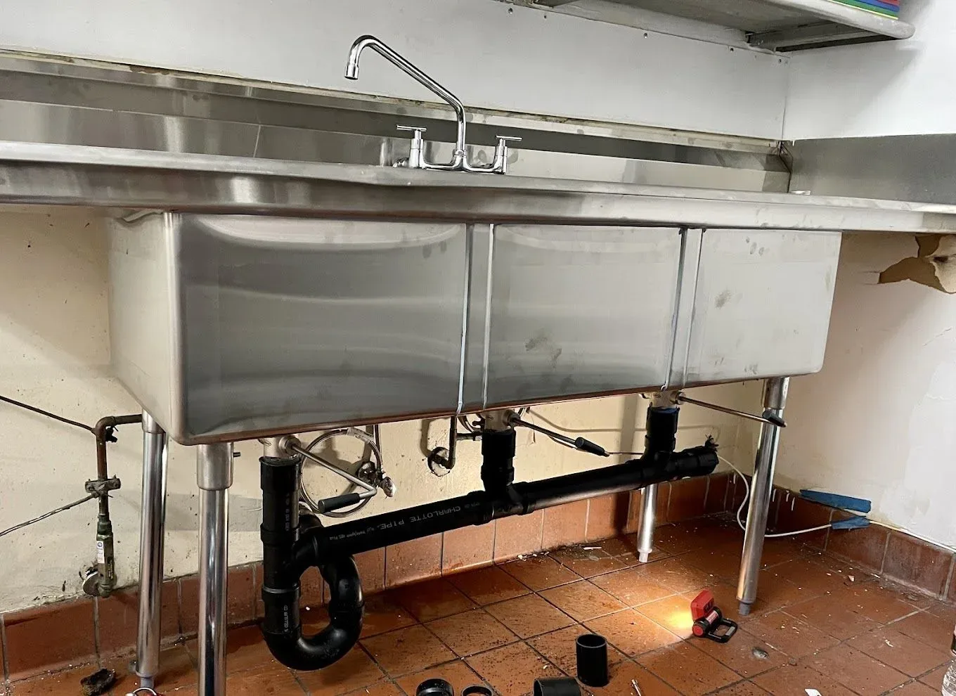 New black drain piping and a P-trap under a stainless steel three-compartment sink