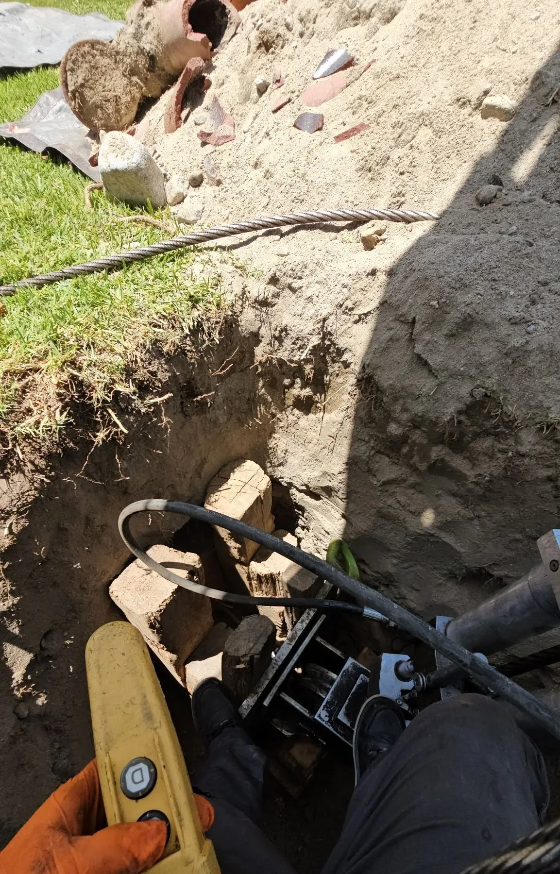 Hydraulic cable pulling rig braced with timber in an access pit, run from a yellow handheld control