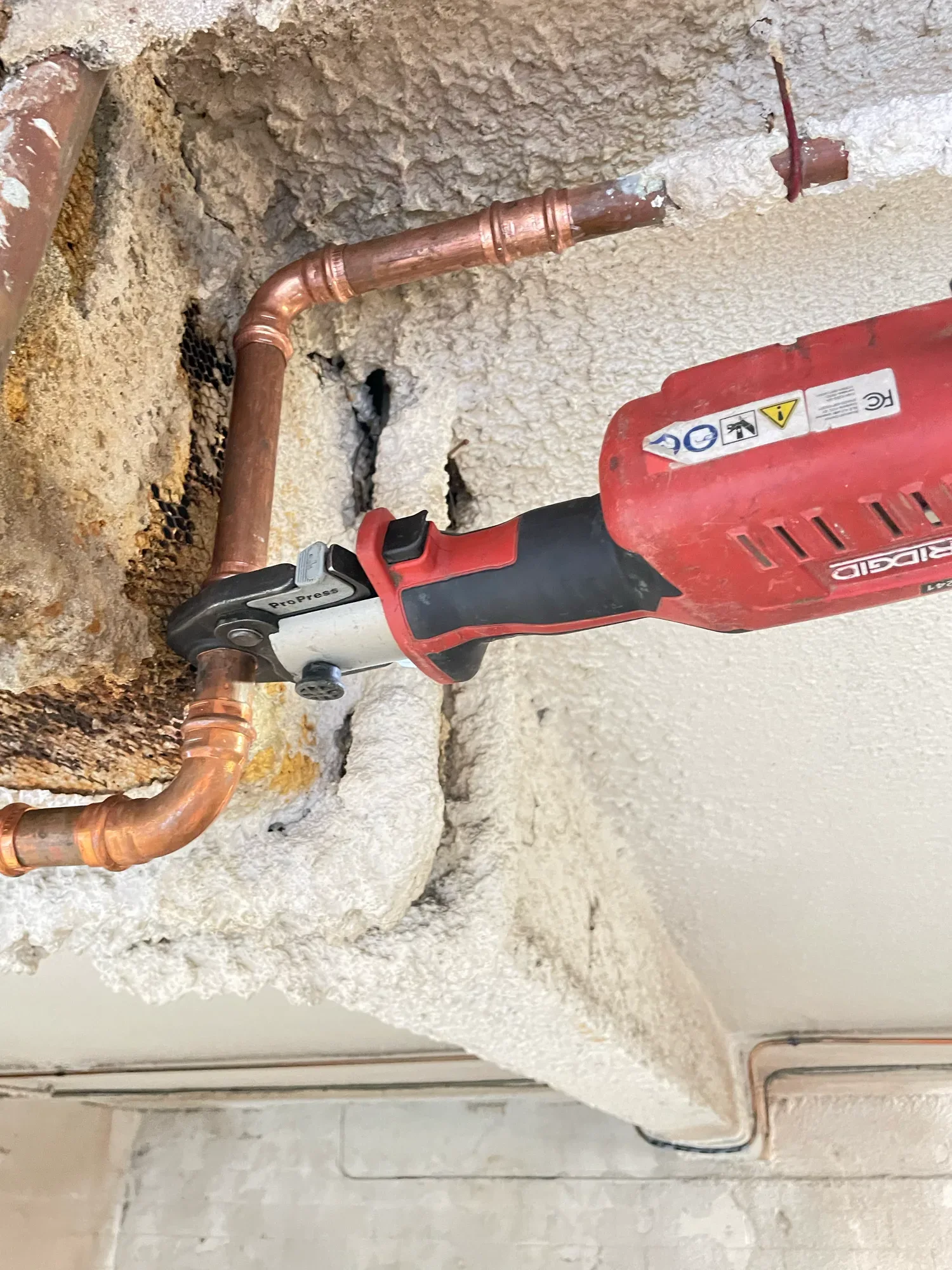 Press tool closing a copper fitting on a water line inside an opened exterior wall