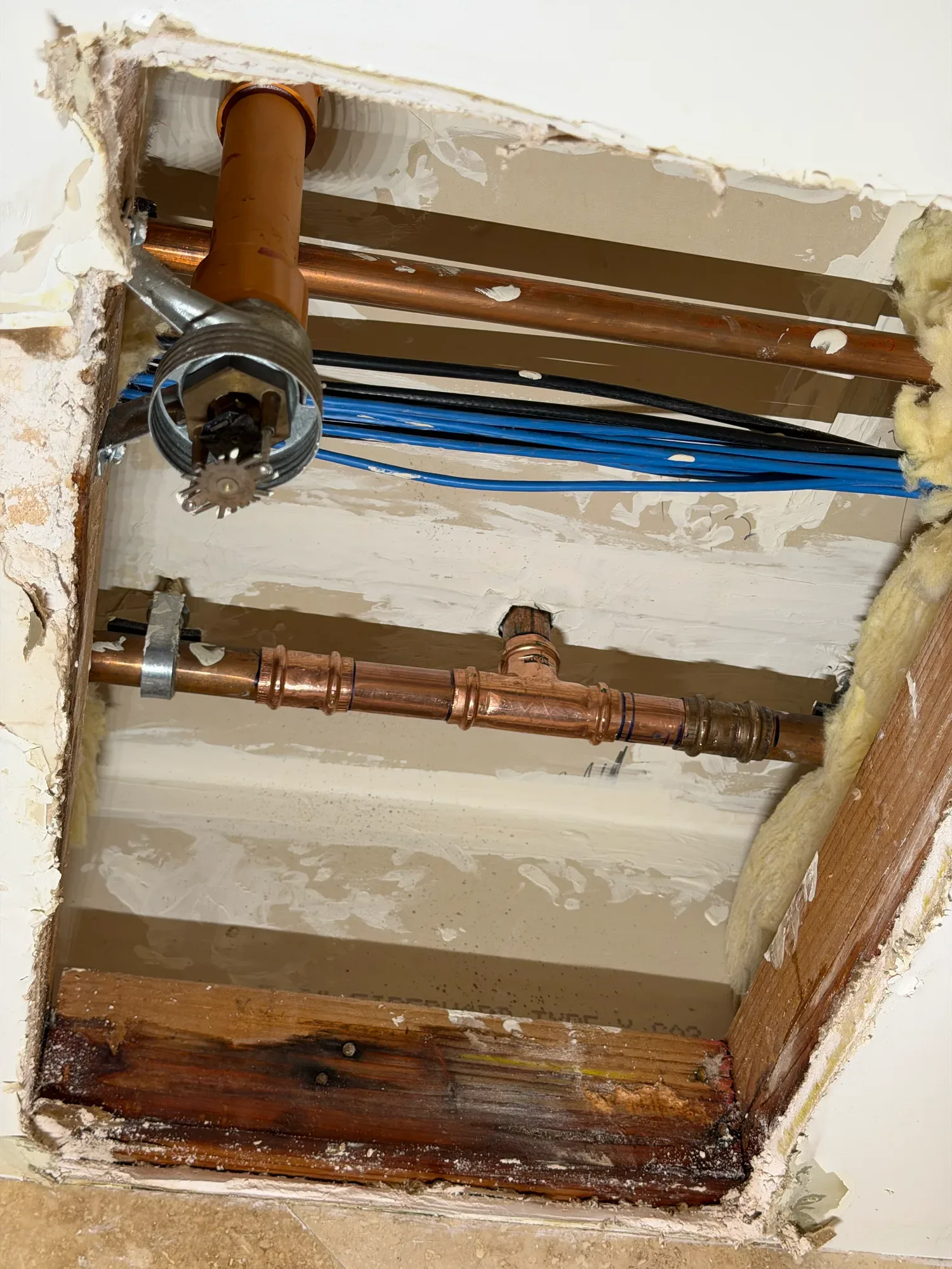 Copper water line with pressed fittings inside an opened ceiling, beside a sprinkler head and stained framing