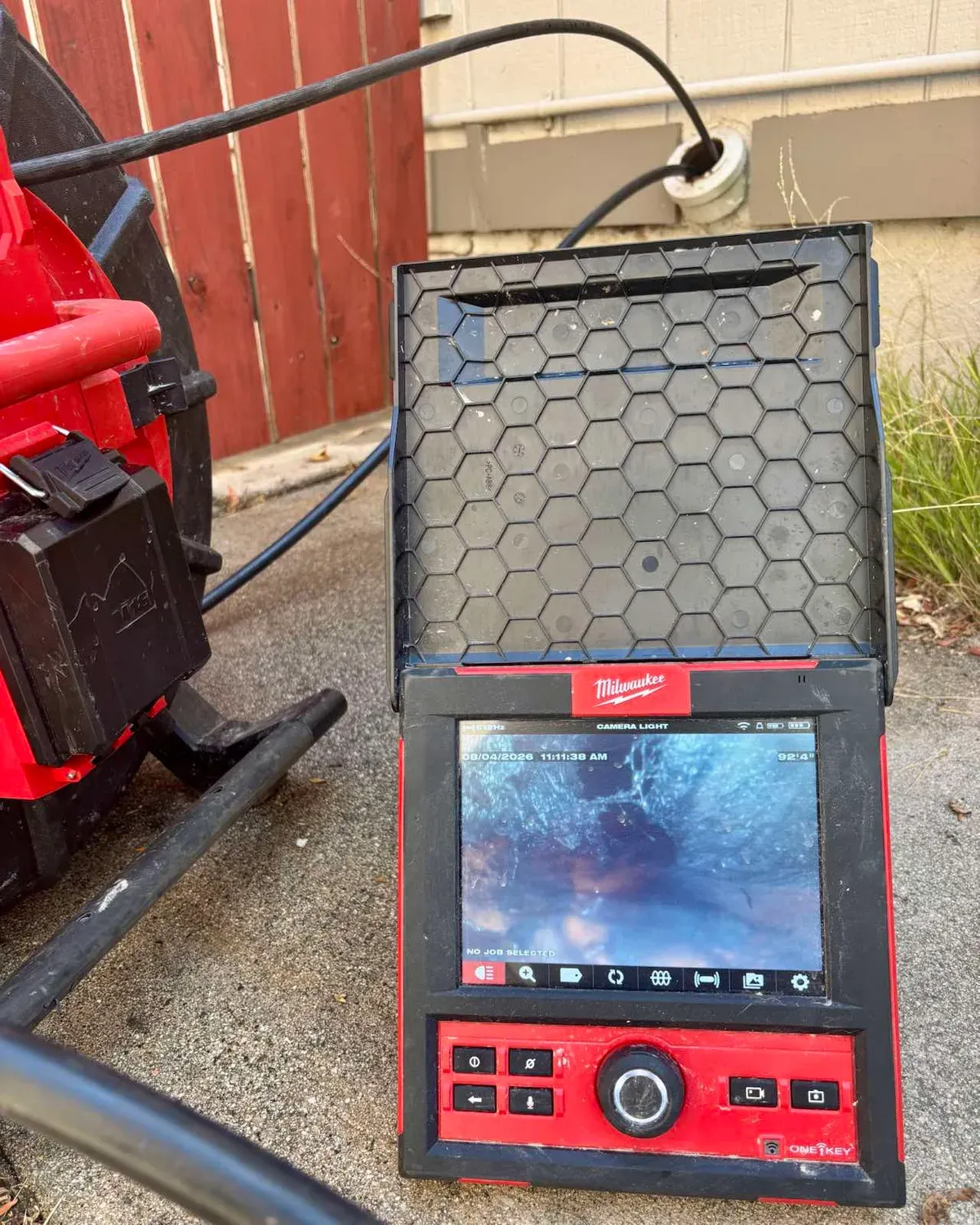A sewer inspection camera monitor at a job, its screen showing live footage from inside the line with the distance reading on screen, and the camera reel beside it
