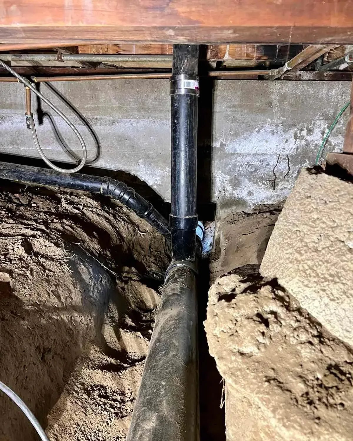 A new ABS sewer line and its vertical riser installed in an open trench in the crawlspace under a raised-foundation home
