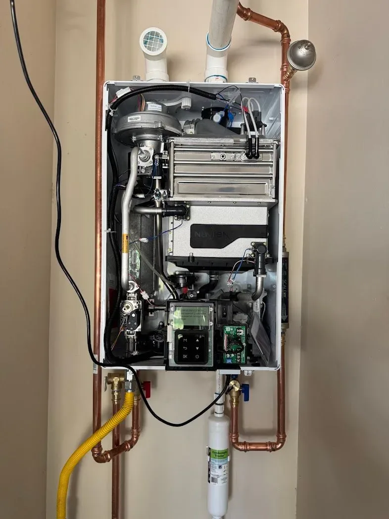 Tankless water heater with its front cover off, plumbed with copper lines and a yellow gas connector