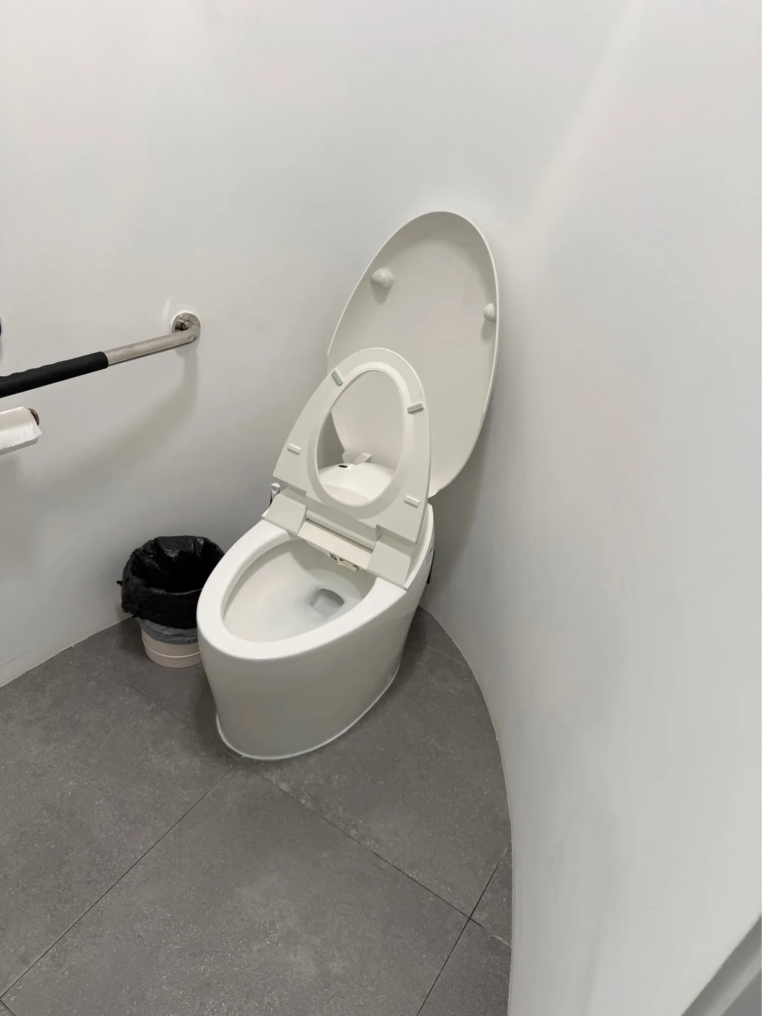 Modern toilet with its seat and lid raised beside a wall grab bar in a small restroom