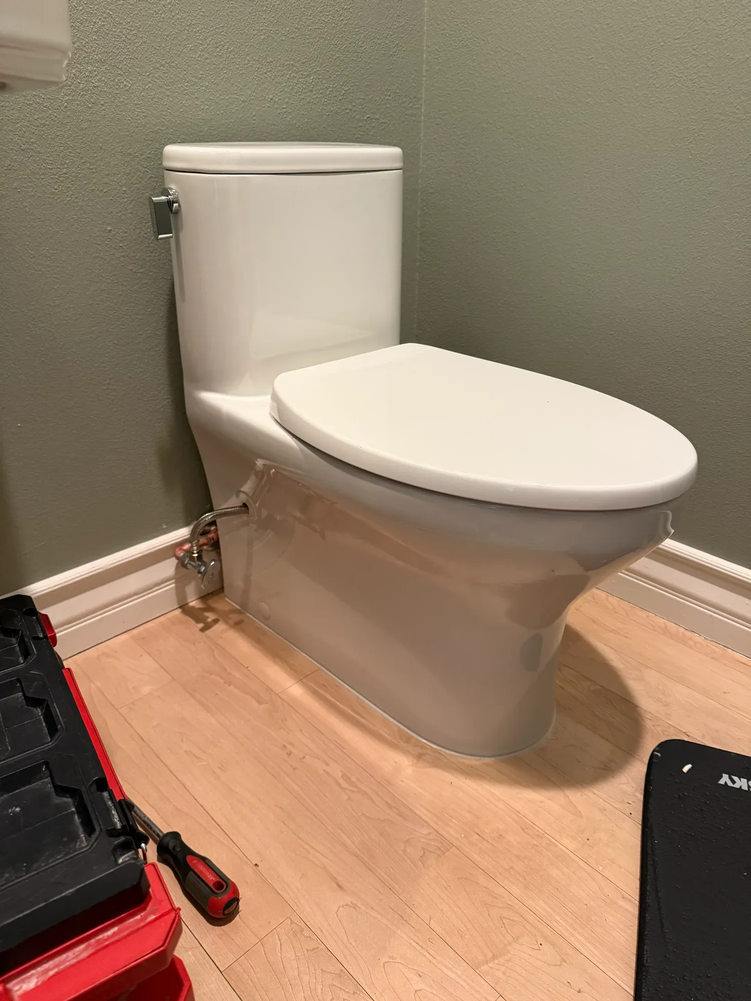 White toilet installed in a small bathroom, with a tool case on the floor beside it