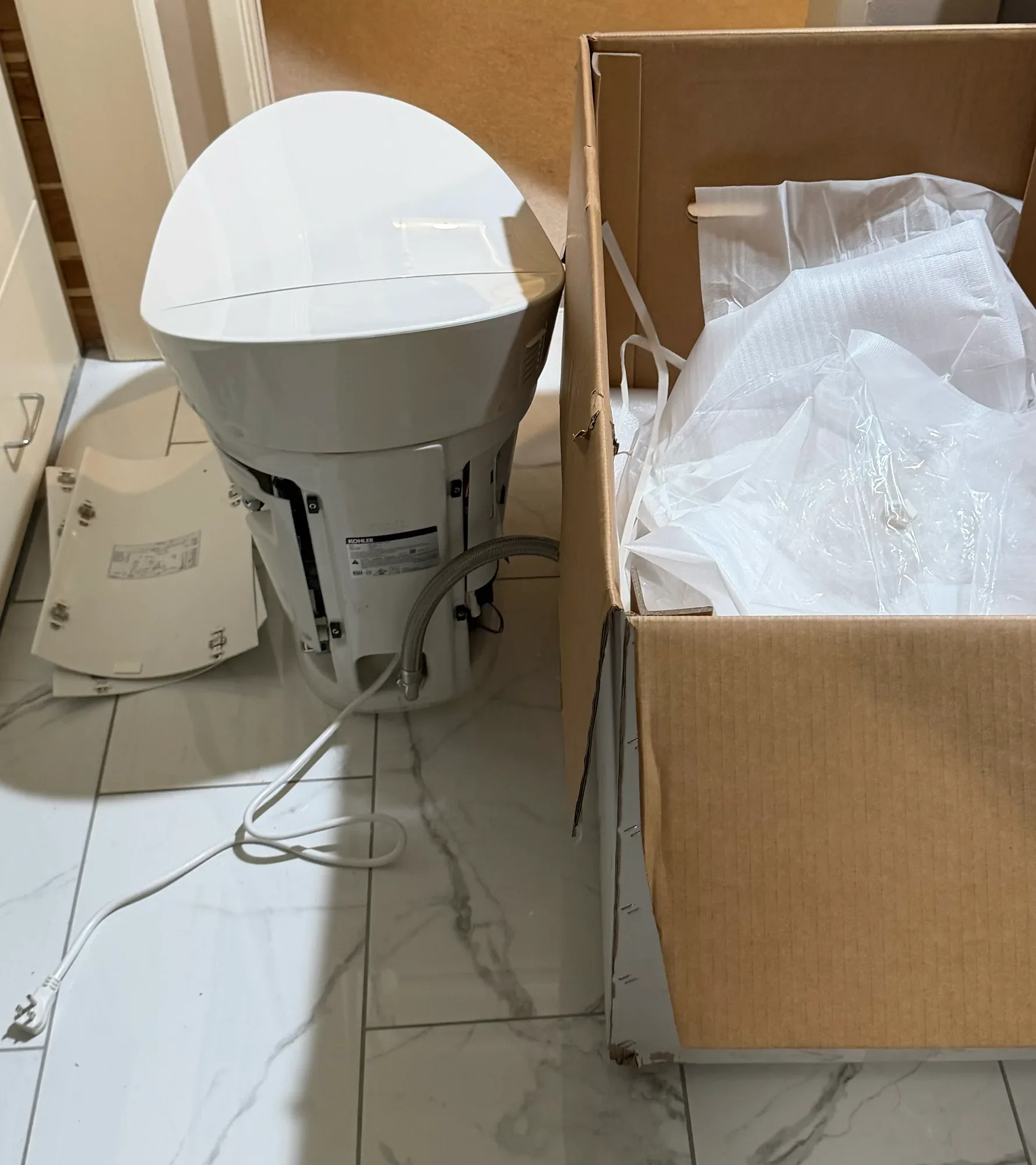 Kohler smart toilet unpacked beside its open box, with the Kohler product label on its back