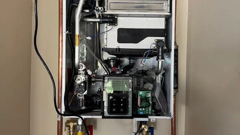 A tankless water heater with its cover removed, showing the heat exchanger and control wiring during service