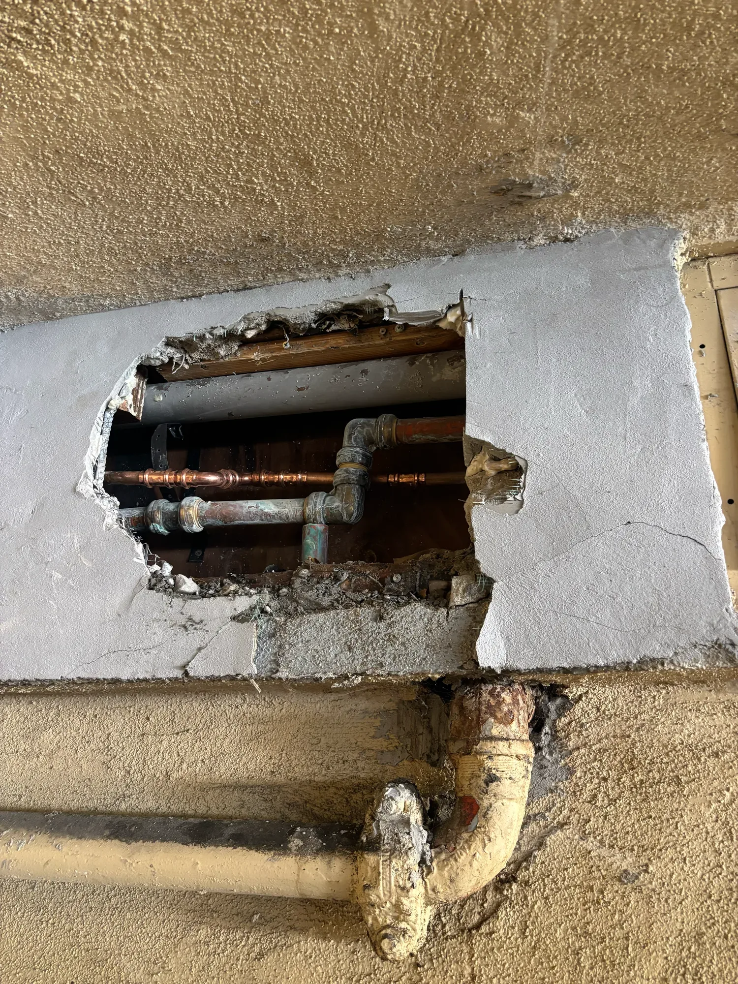 Copper and older water lines exposed through a hole cut in a patched stucco wall