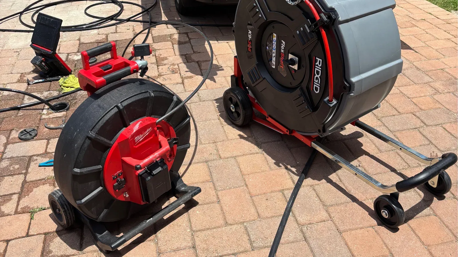 Two drain cleaning machines with coiled cables staged on a paver driveway